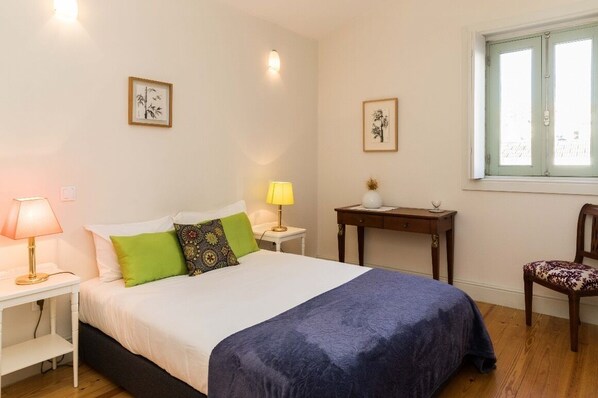 A bedroom with a bed, two bedside tables, a chair, a window, and two wall-mounted lamps.