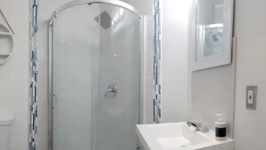 Een badkamer met een glazen douchecabine, een witte wastafel met spiegel erboven en een toilet aan de linkerzijde.
