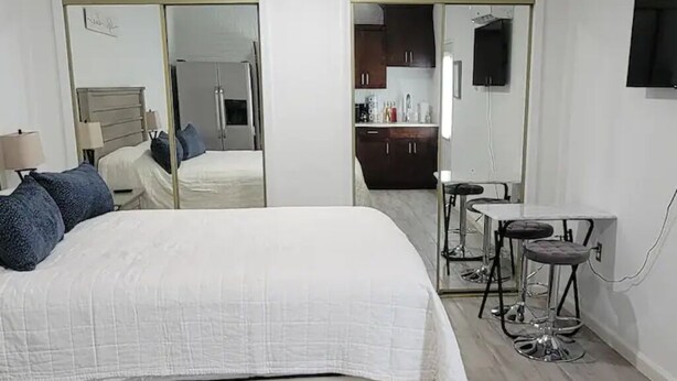 Een slaapkamer met een groot bed, een spiegel, een kleine keukenhoek en een televisie.
