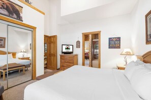 Quarto de hotel com uma cama grande, penteadeira de madeira, televisão e espelho.