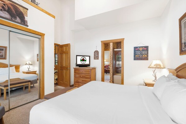 A hotel room with a large bed, a wooden dresser, a television, and a mirror.