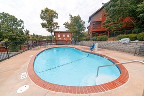 Piscina com borda de tijolos, rodeada por espreguiçadeiras e um cercado.