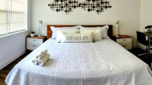 A neatly made bed with a white bedspread and pillows, including one with the text "LOVE LIVES HERE". - Amazing Melly's (Tampa)