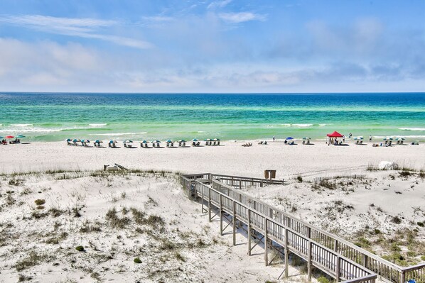 A beach with a wooden boardwalk leading to the water, beach umbrellas, and a few people.