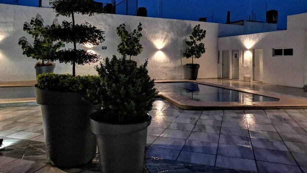An outdoor pool area with potted plants and a white wall with a light fixture.