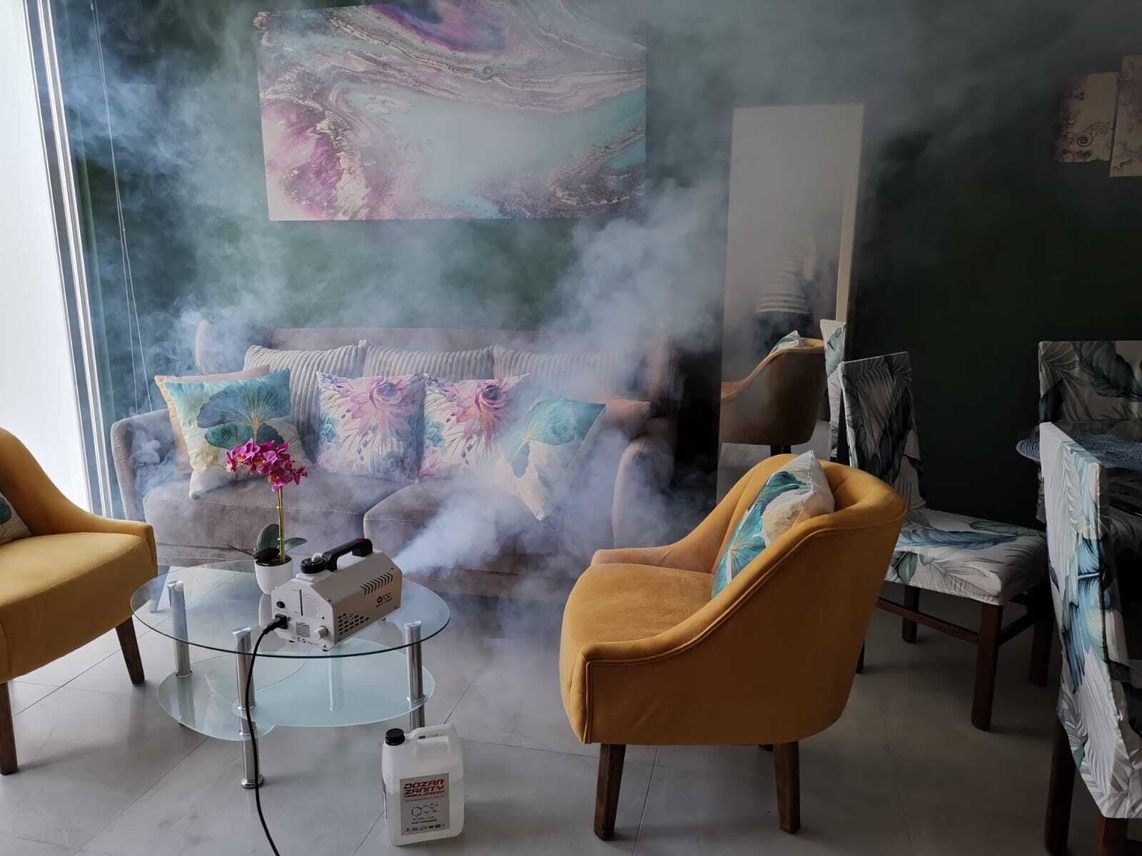 Una habitación con sofá, sillones y una mesa de vidrio con un dispositivo y un recipiente.