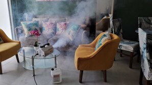 A room with a sofa, armchairs, and a glass table with a device and a container.