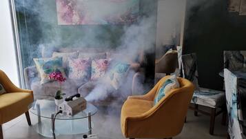 Una habitación con sofá, sillones y una mesa de vidrio con un dispositivo y un recipiente.