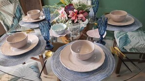 A dining table set with plates, bowls, and blue glassware, surrounded by chairs with floral upholstery.