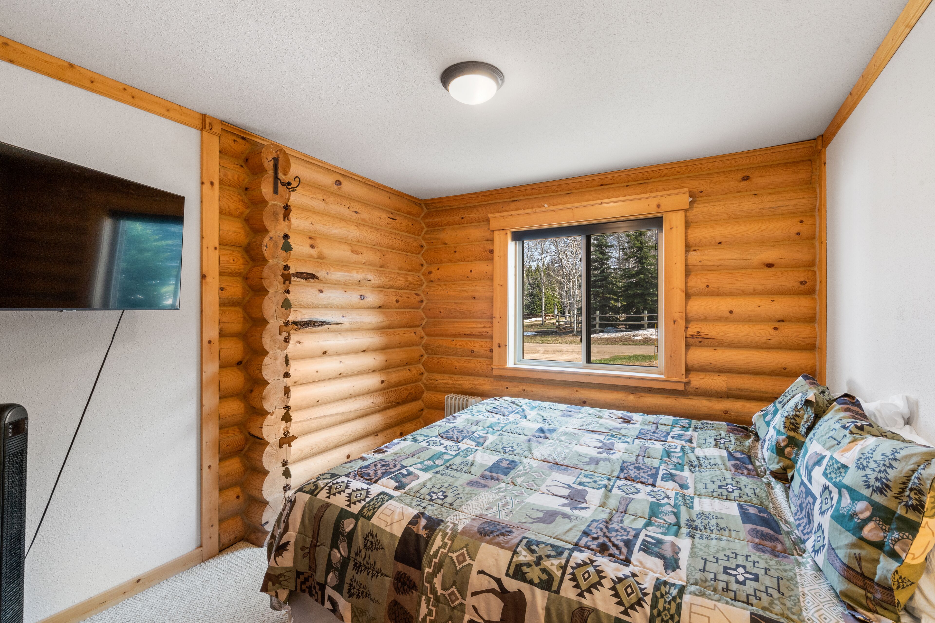 A log cabin bedroom with a bed, a window, and a ceiling light.