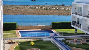 Ett poolområde med utsikt över havet, en modern byggnad och en vackert anlagd tr ädgård.