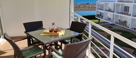 A balcony with a table and chairs, a yellow umbrella, and a view of the sea and buildings.