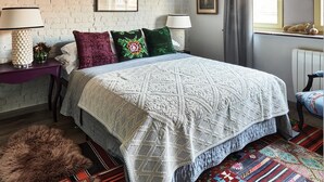 A bedroom with a large bed, a brick wall, a window with curtains, and a nightstand with a lamp. - Charming 2-bedroom Home & Garden (Brussels)