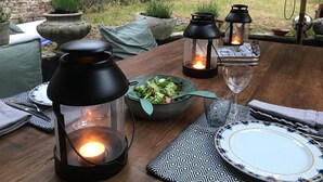 A wooden dining table with a bowl of salad, two black lanterns, a wine glass, and a plate. - Charming 2-bedroom Home & Garden (Brussels)