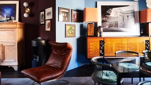 A modern living room with a brown leather chair, a glass-top coffee table, and a dining area with a wooden cabinet and chairs. - Charming 2-bedroom Home & Garden (Brussels)