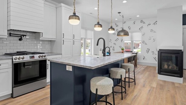 A modern kitchen with white cabinetry, a central island with stools, pendant lighting, and a fireplace. - Mountain Home near Lakes w/Hot Tub & Putting Green (Heber City)