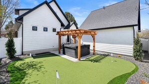 A residential backyard with a wooden pergola, artificial turf, and a garage. - Mountain Home near Lakes w/Hot Tub & Putting Green (Heber City)