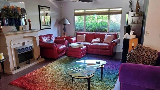 A living room with a fireplace, red leather sofa, glass coffee table, and a colorful rug. - Colorful Warm Weather Jewel House 10,000 sq ft lot. (Menifee)