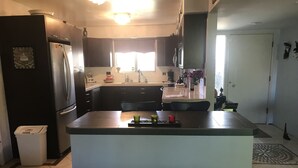 A modern kitchen with a central island, dark cabinetry, and a refrigerator. - Colorful Warm Weather Jewel House 10,000 sq ft lot. (Menifee)