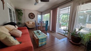 A living room with a red sofa, a wooden coffee table, and a dining table with chairs. There are potted plants and a ceiling fan. - Colorful Warm Weather Jewel House 10,000 sq ft lot. (Menifee)