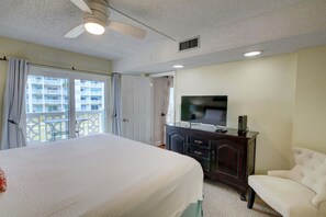 Ein Hotelzimmer mit einem großen Bett, einem Fernseher, einem Schminktisch und einem Balkon mit Blick auf das Gebäude.
