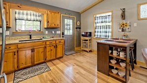 A kitchen with wooden cabinets, a granite countertop, a refrigerator, a microwave, and a dining area with a table set for two. - Beary’s Den where Chic meets Country in this Cozy Cabin (Murphy)