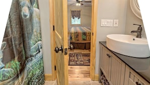 A bathroom with a wooden door, a white sink, and a patterned rug. - Beary’s Den where Chic meets Country in this Cozy Cabin (Murphy)