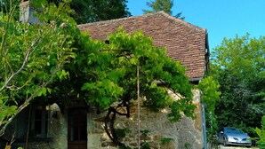 A rustic stone building with a tiled roof, a wooden door, and a gravel driveway. - Quercy house at the foot of the cliffs (Vayrac)