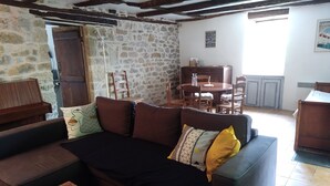 A cozy living room with a stone wall, wooden furniture, and a dining area with a table and chairs. - Quercy house at the foot of the cliffs (Vayrac)