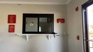 Una zona de recepció amb una finestra, un detector d'incendis i diversos senyals informatius a la paret.