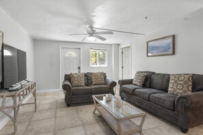 Ein Wohnzimmer mit zwei Ledersofas, einem Glastisch, einem Deckenventilator und einem Fernseher.