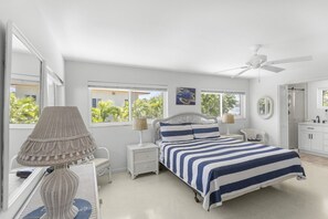 A bedroom with a bed, nightstands, a lamp, a ceiling fan, and a view of the outdoors.