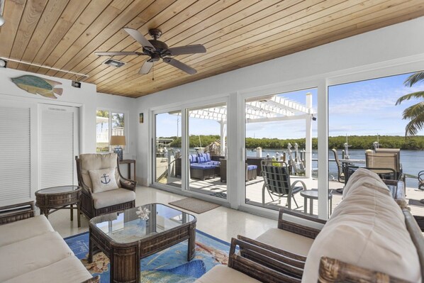 A spacious indoor area with a ceiling fan, large windows, and a view of the water outside.