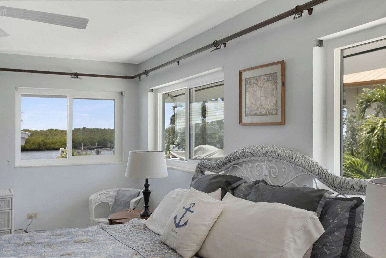 Une chambre à coucher comprenant un lit, une chaise, une lampe et deux fenêtres donnant sur un paysage verdoyant.