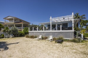Ein Anwesen am Strand mit überdachter Terrasse, Liegestühlen und Meerblick.