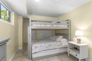Un lit superposé avec un lit inférieur, une table de chevet avec une lampe et une fenêtre donnant sur des palmiers.