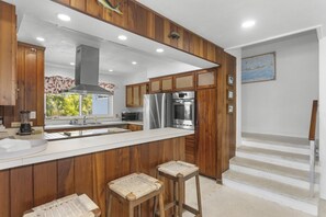 A modern kitchen with wooden cabinetry, stainless steel appliances, a large island, and a view of the outdoors.