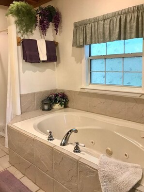 Ein Badezimmer mit einer freistehenden Badewanne, einem Fenster mit einem grünen Vorhang und einer Topfpflanze an der Wand.