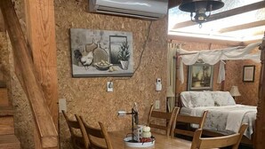 Un coin repas rustique en bois, avec une table et des chaises, un tableau accroché au mur et, au fond, un lit à baldaquin.