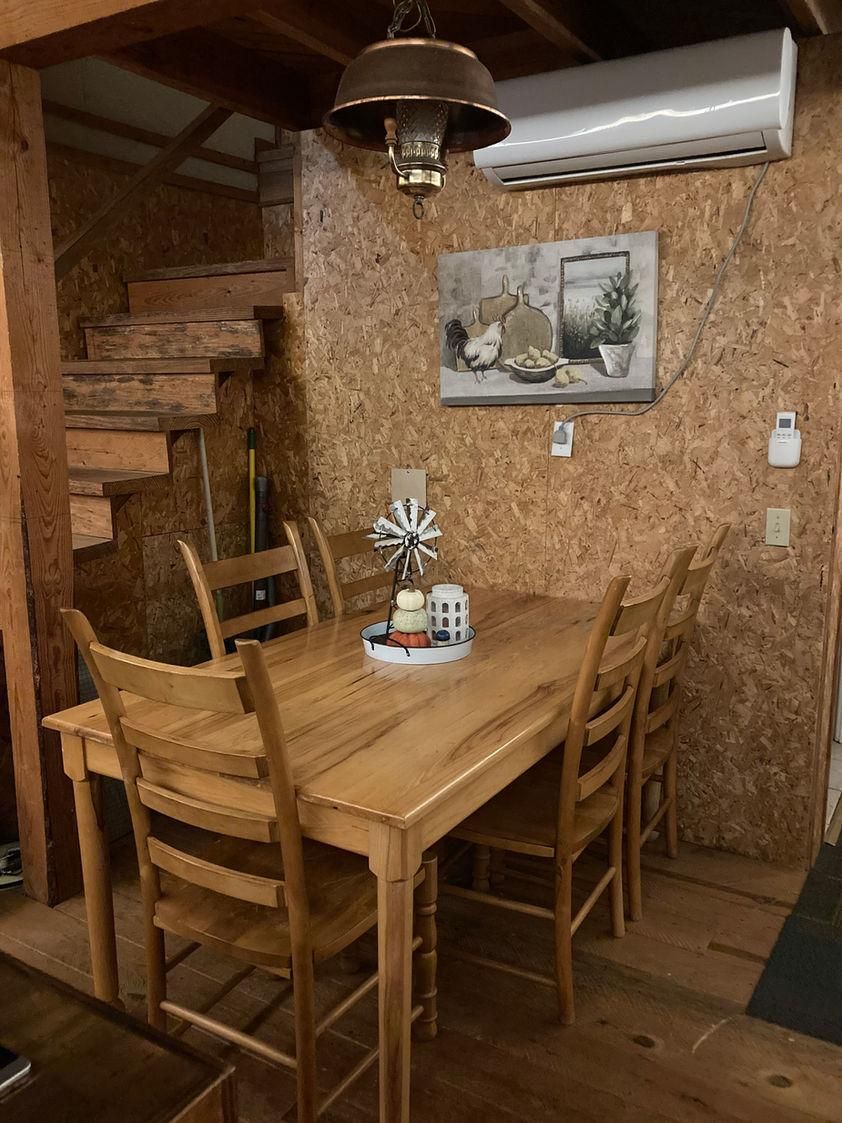 A wooden dining table with chairs, a hanging light fixture, and a painting on the wall.