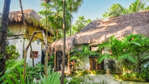 A tropical garden with a thatched-roof hut, surrounded by lush greenery and palm trees. - Yaxchen Tulum Cabañas & Cenote (Tulum)