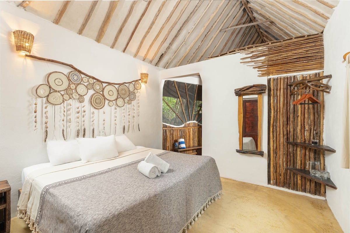 A bedroom with a bed, a wall hanging, a wooden shelf, and a door.