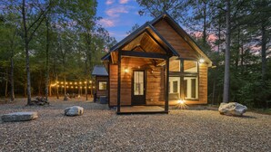Een houten chalet met een veranda, omgeven door bomen en een grindpad.