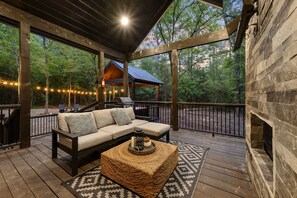 A covered deck with a sofa, a woven ottoman, and a patterned rug.