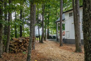 A rustic cabin surrounded by tall trees, a stack of firewood, and a clear view of the sky.