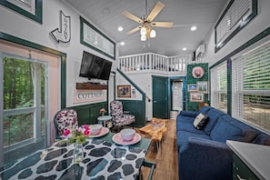 A cozy cottage interior with a staircase, a television, a dining area with a table and chairs, and a blue sofa.