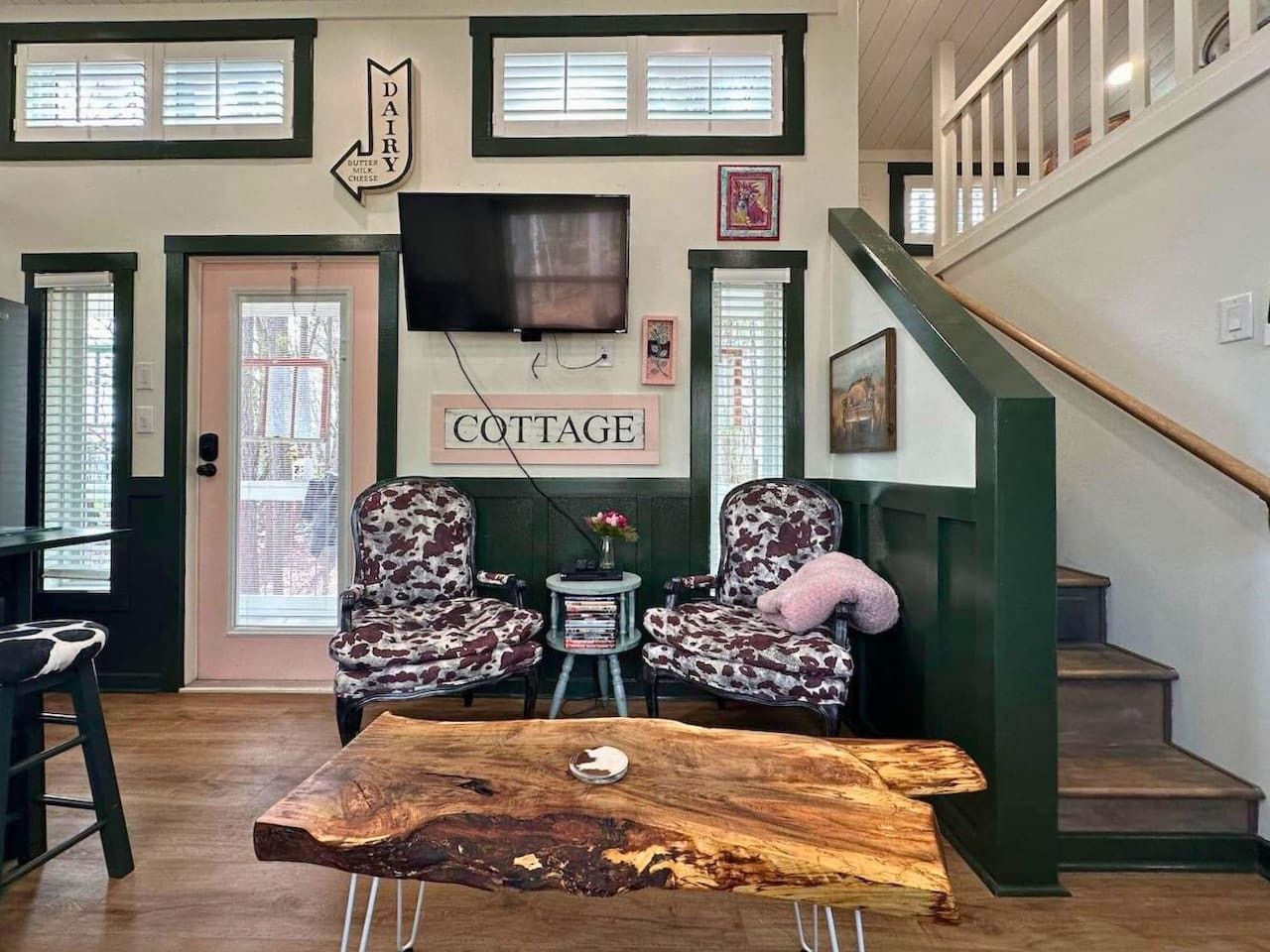 Un intérieur chaleureux avec une table basse en bois, deux fauteuils à motifs, une petite table d’appoint avec des livres et un escalier doté d’une rampe verte.