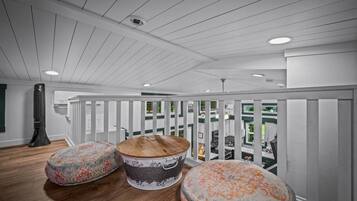 A spacious balcony with a white railing, a large fan, and three round ottomans with floral patterns.