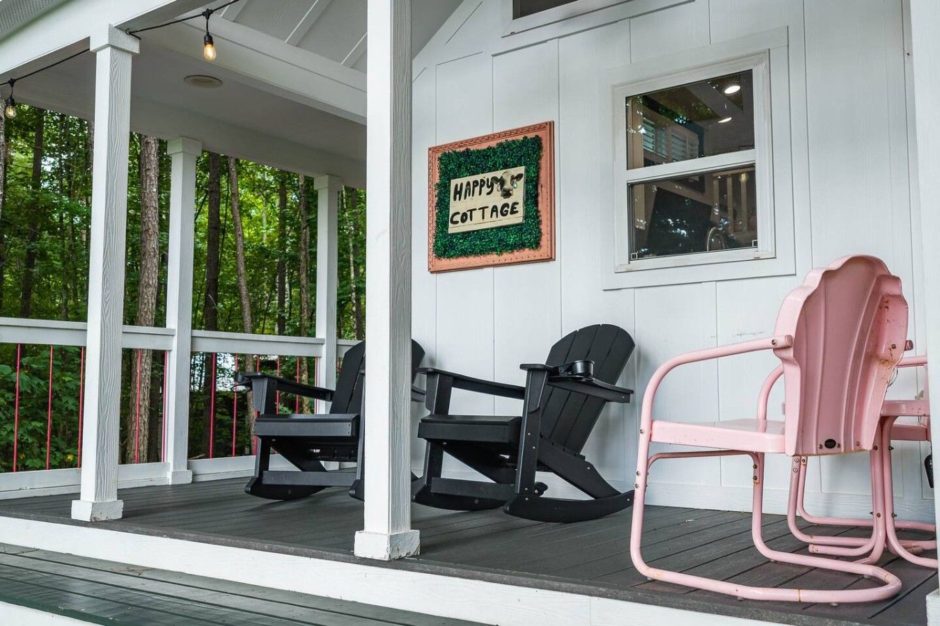 Un porche con sillas Adirondack, un letrero que dice 'HAPPY COTTAGE' y una ventana.