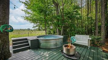 A hot tub on a wooden deck surrounded by trees, with a bench and steps leading up to it.
